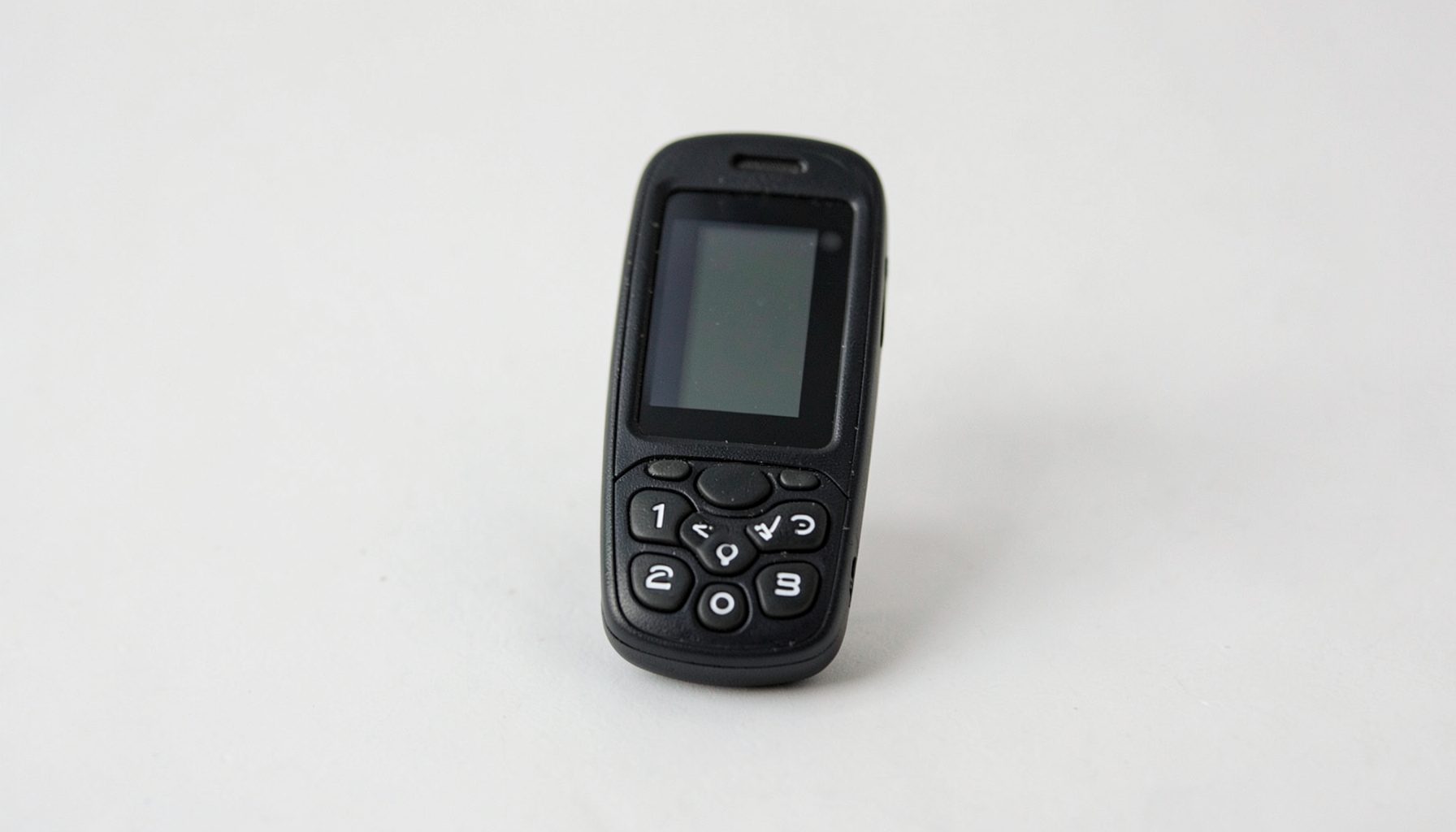 A small black candy-bar phone with a compact screen and raised numeric buttons, shot against a plain light backdrop.