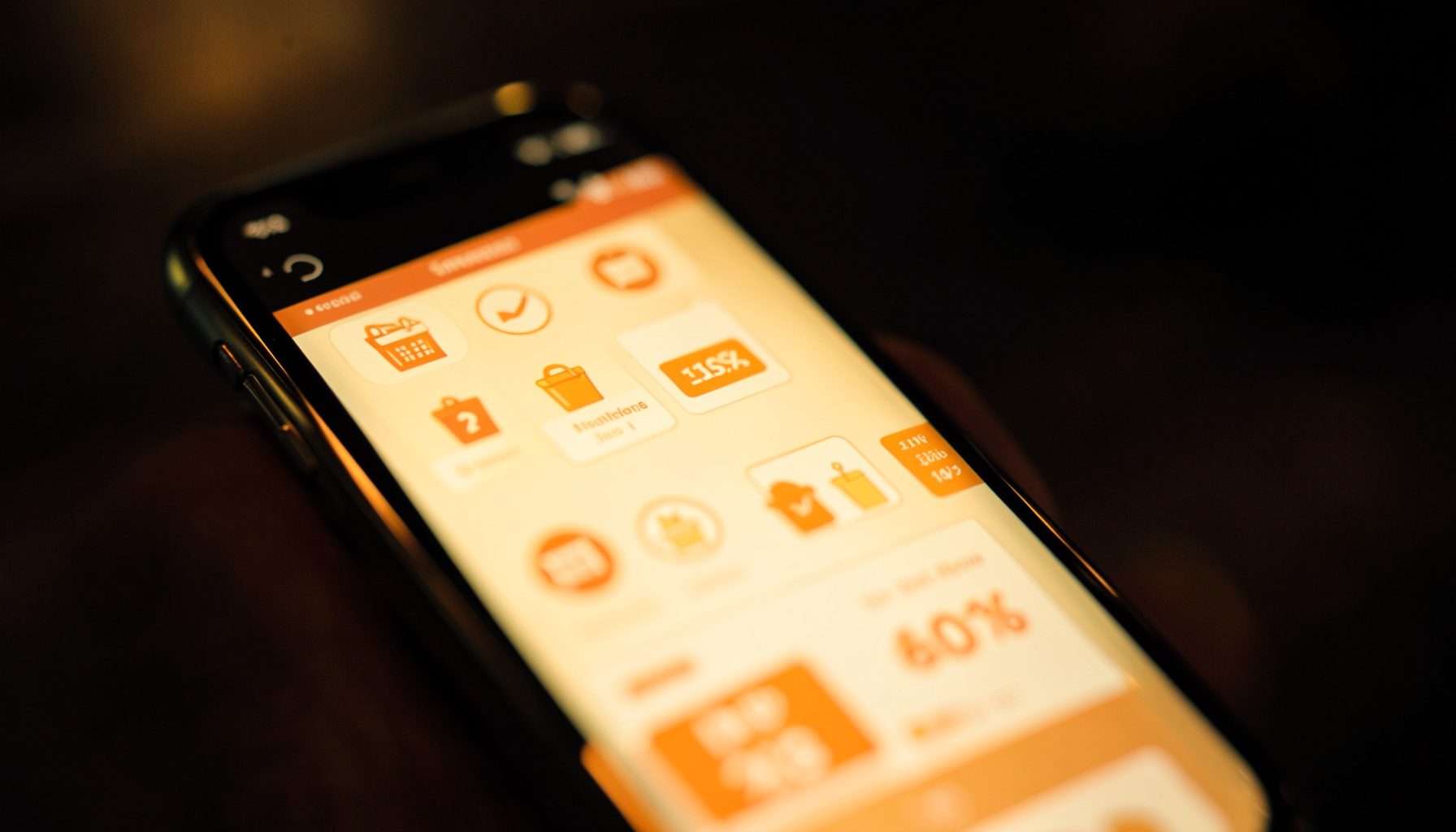 A warm, softly lit close-up of a smartphone screen displaying shopping icons and discount tags, with rich amber and cream tones against a dark blurred background